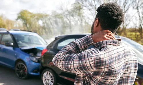 Young man rubbing neck in pain from whiplash injury standing by damaged car after a traffic accident.