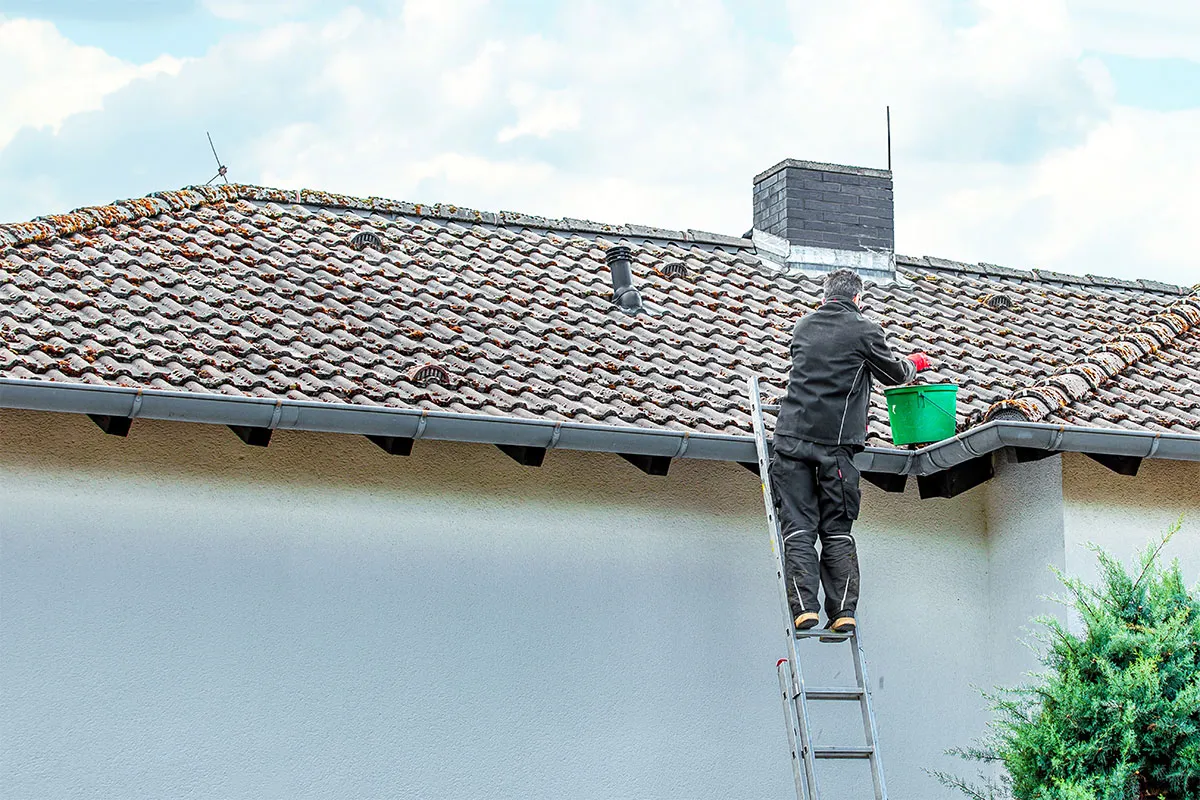 A gutter cleaning technician is placing debris from the rain gutter into a bucket, allowing stormwater to move through freely.
