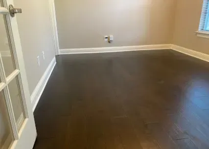 Clean white baseboards being installed to match freshly laid hardwood flooring.
