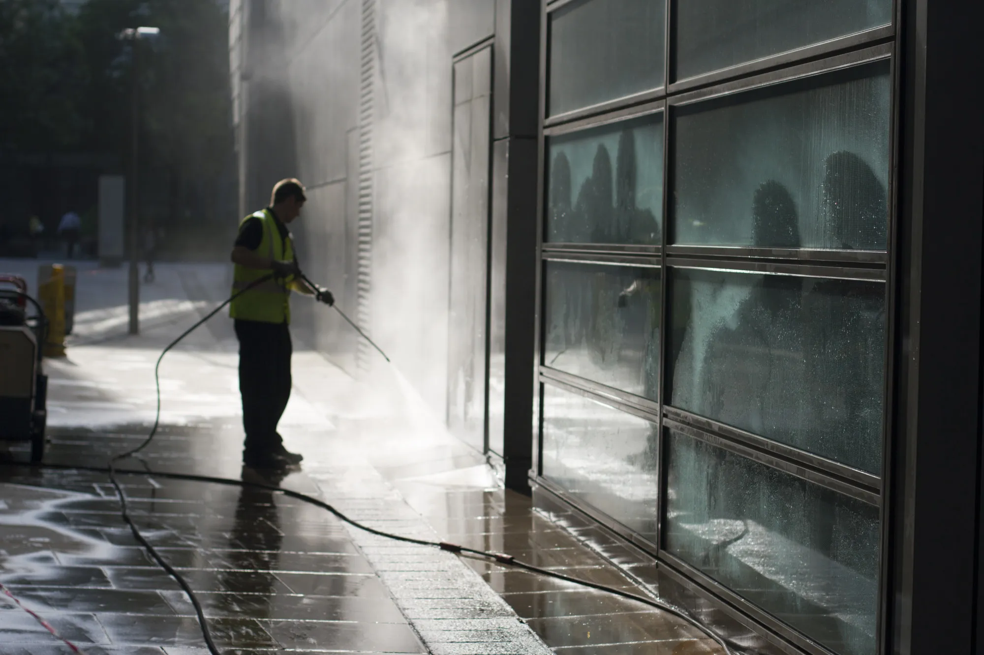 A professional pressure washing technician is performing power washing services for a commercial space.