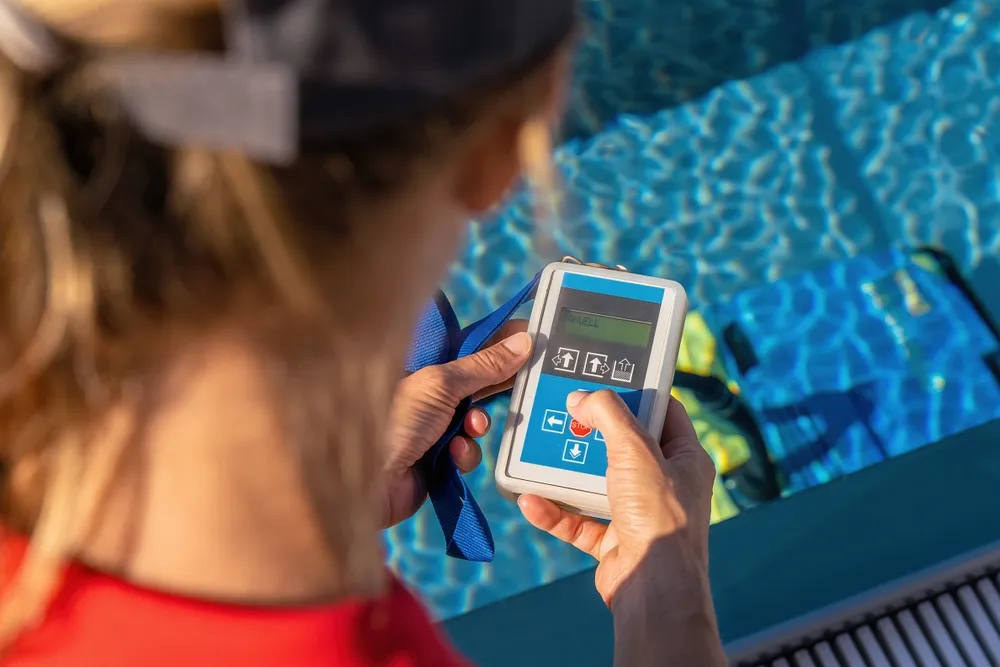 Close-up of a lifeguard operating a digital pool control device next to a clear blue swimming pool.