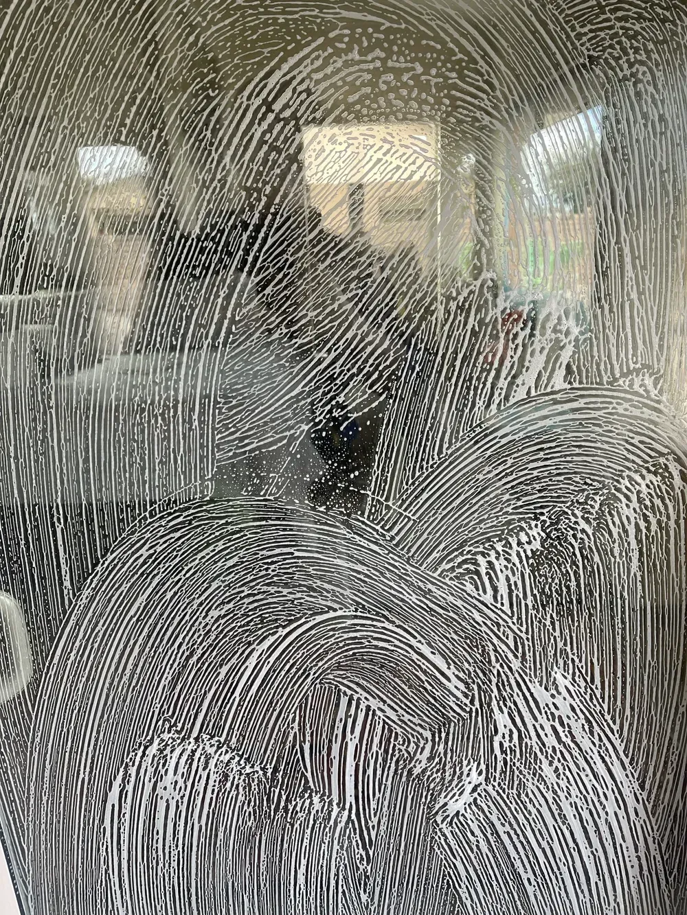 A window covered in soapy water applied by a window washer using dawn dish soap and a microfiber cloth to ensure a streak free finish.