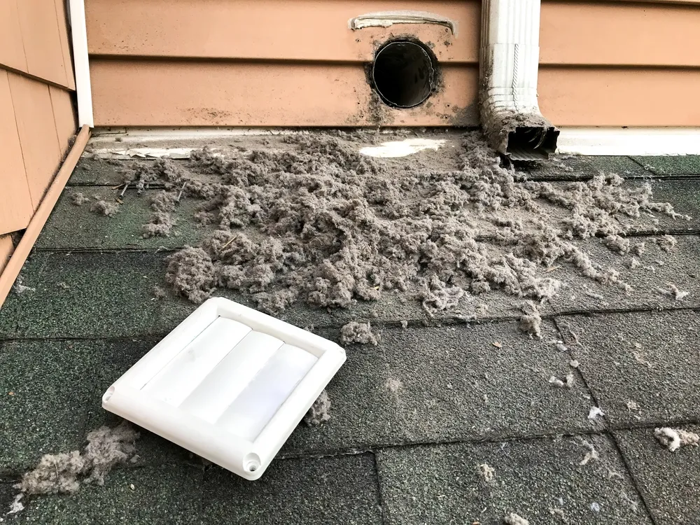 A technician removing built-up lint from a dryer vent in a Birmingham home.