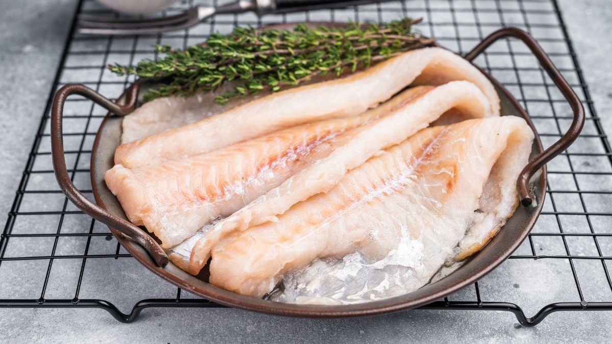 Filés de bacalhau crus e ramos de tomilho fresco em uma bandeja sobre uma grelha.