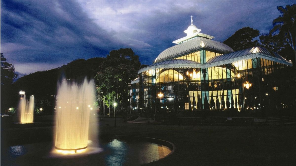 O Palácio de Cristal, em Petrópolis, é um destaque da serra fluminense, combinando história e beleza noturna para o turismo de inverno. Palácio de Cristal iluminado à noite, com fontes jorrando água e céu escuro.