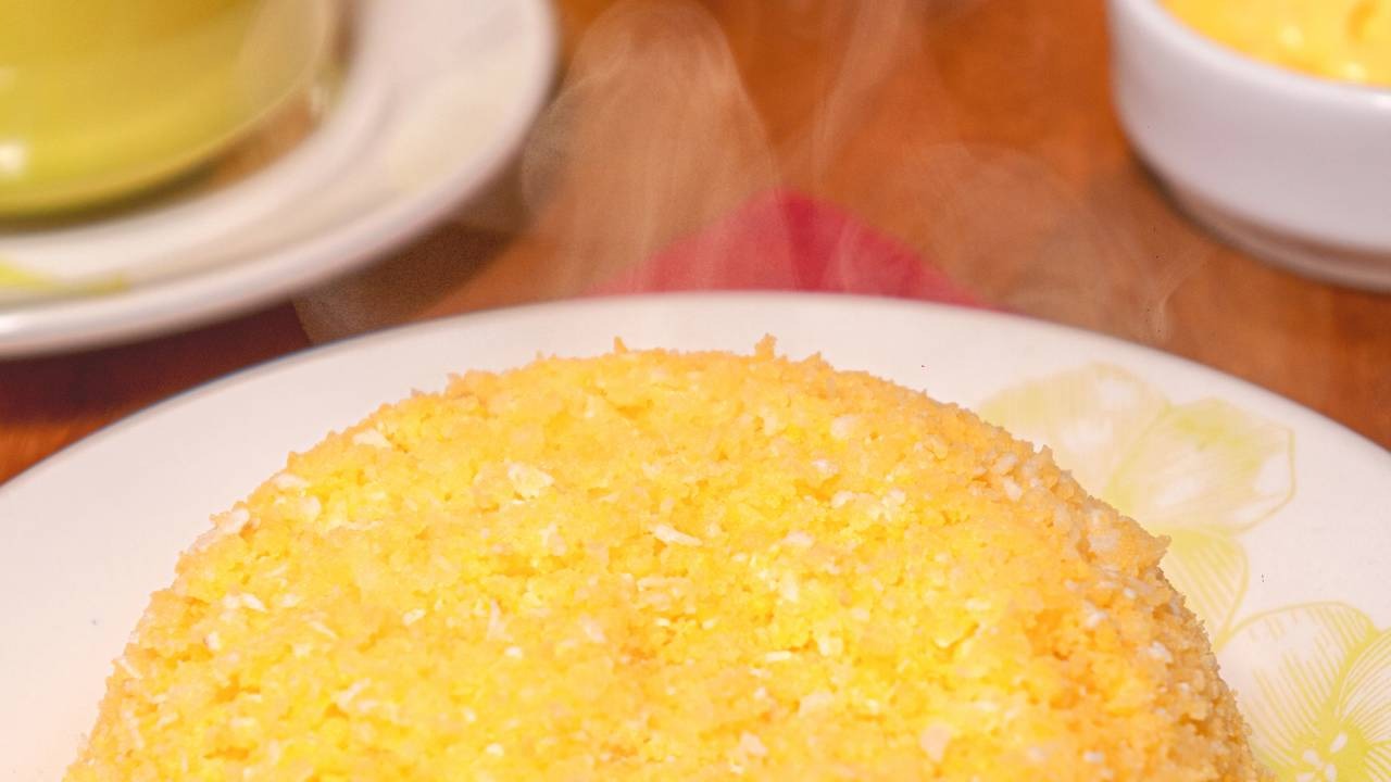 Comece o domingo com um café da manhã variado e nutritivo, incluindo uma porção de cuscuz de milho para repor energias. Porção de cuscuz de milho amarelo e branco fumegando em prato decorado