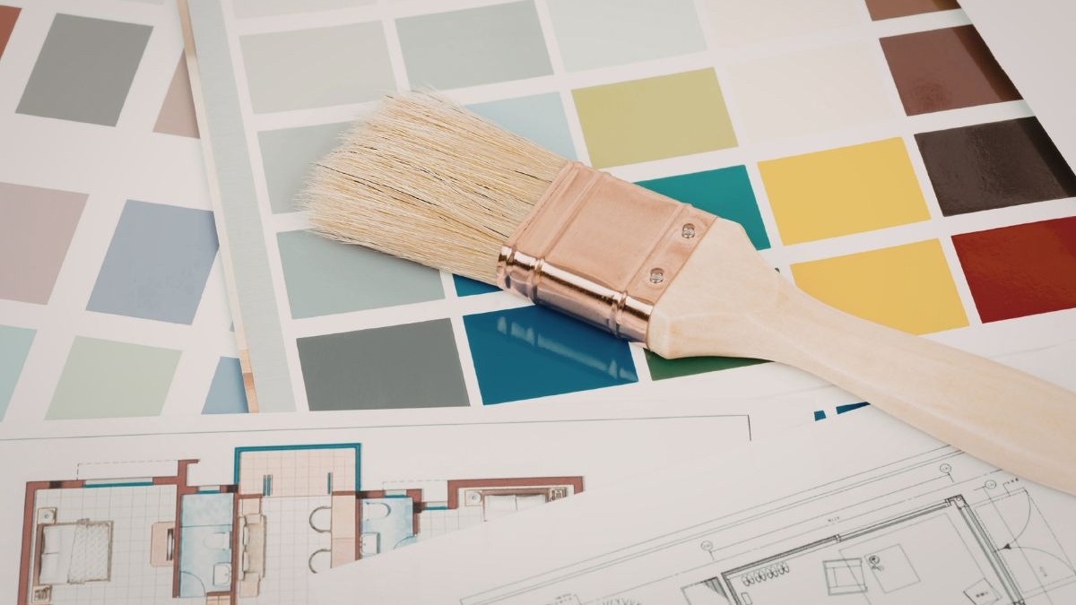 Pincel de pintura sobre cartelas de amostras de cores e plantas baixas de arquitetura.