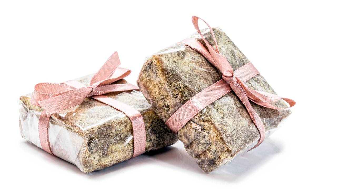 A palha italiana, uma sobremesa versátil e fácil de preparar, agrada a todos e pode gerar renda extra. Duas palhas italianas embrulhadas em plástico com fitas rosas sobre fundo branco