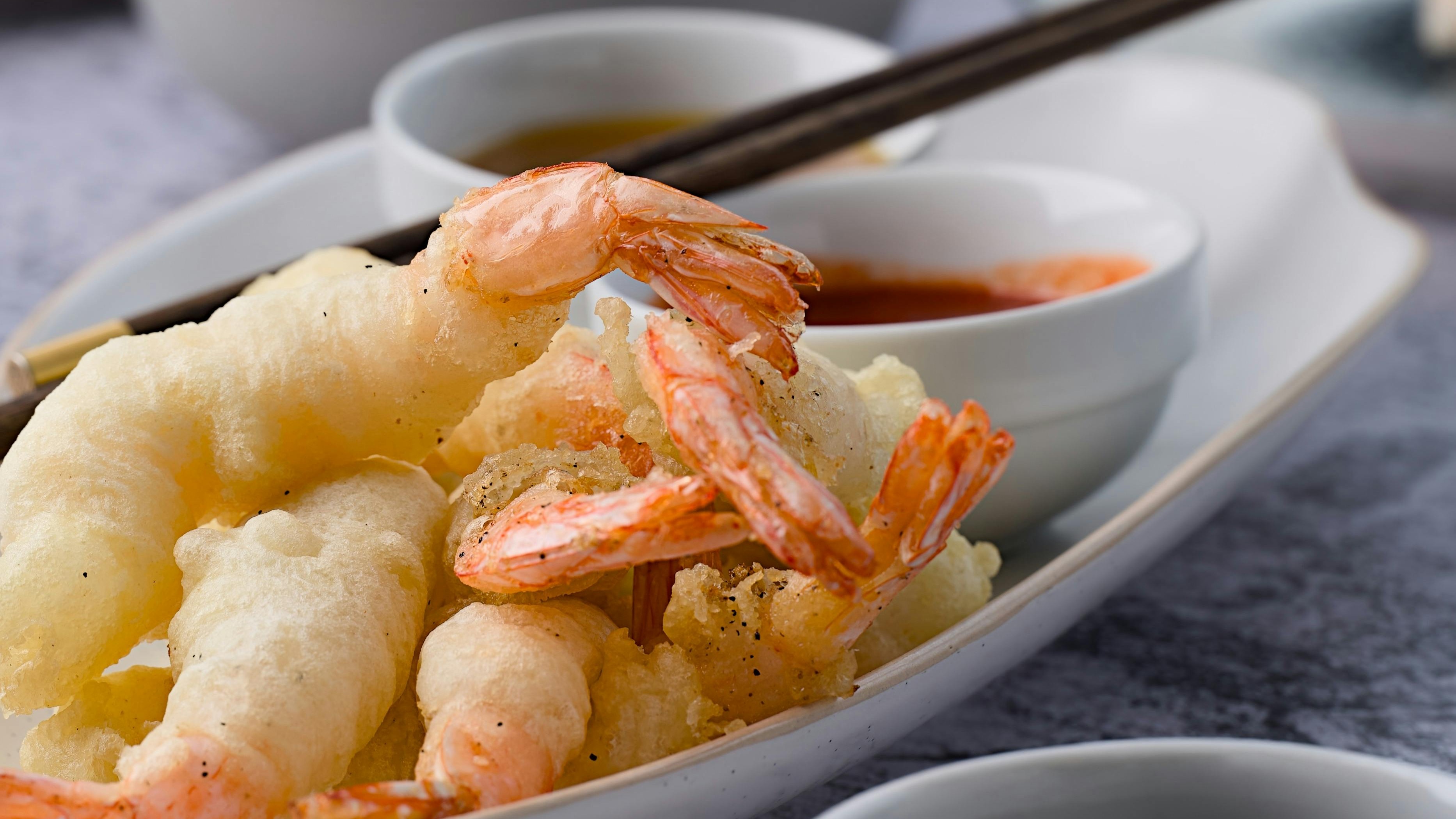 Tempura de camarão e vegetais fritos em massa crocante, servidos com molho e hashi.