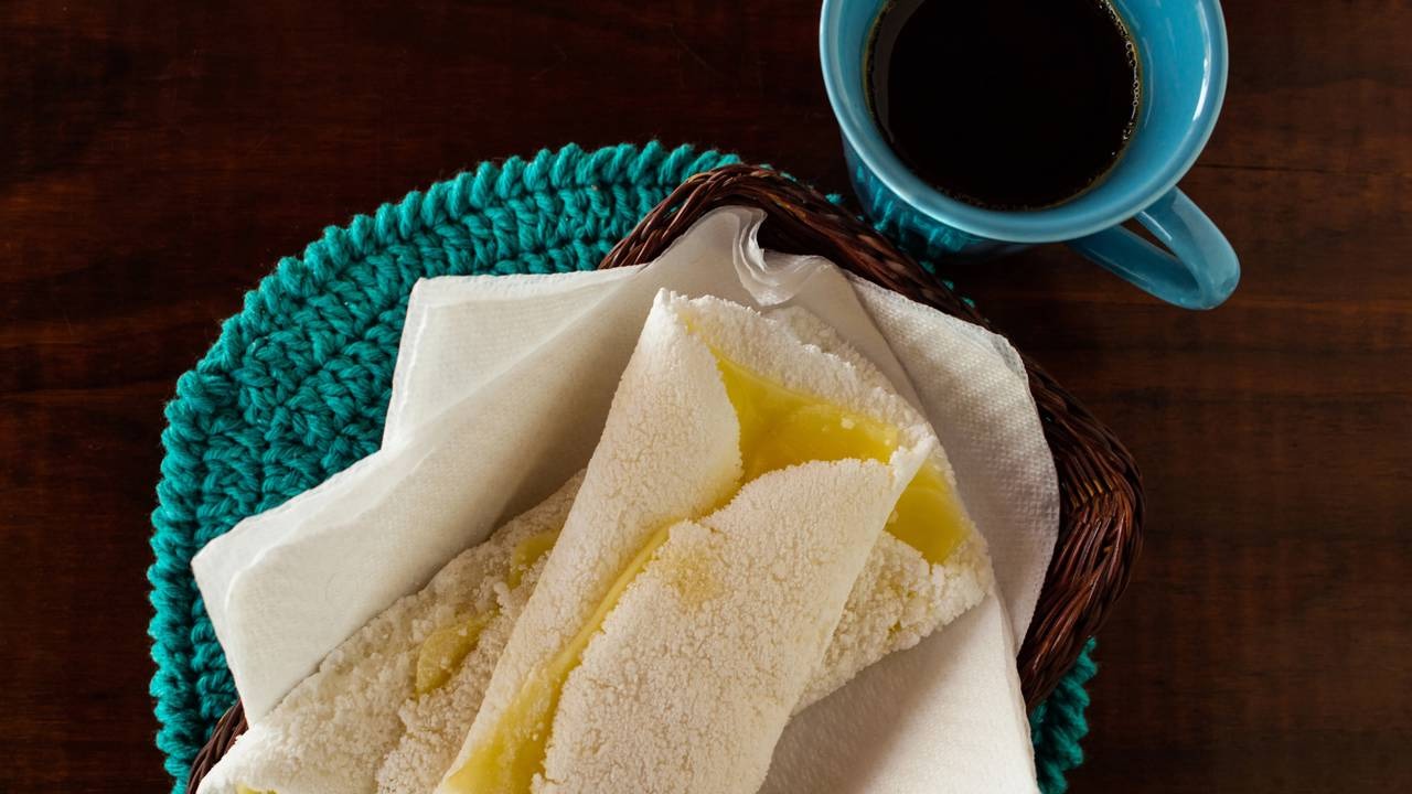 Para um café da manhã ou lanche nutritivo, as tapiocas fit se apresentam como uma alternativa versátil e saborosa. Duas tapiocas recheadas em cesta, com xícara de café azul em mesa de madeira