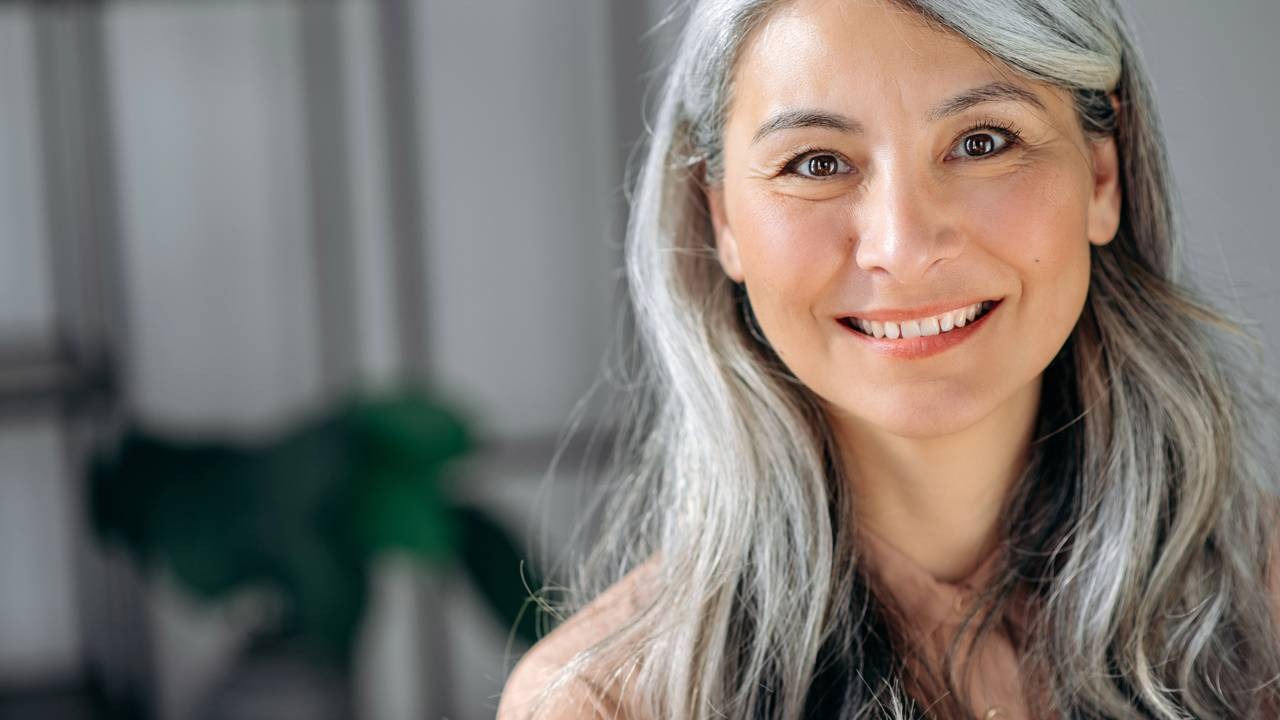 Manter os cabelos brancos em dia exige atenção a detalhes e técnicas para um resultado perfeito em casa. Close-up de mulher sorridente com longos cabelos grisalhos e olhos castanhos