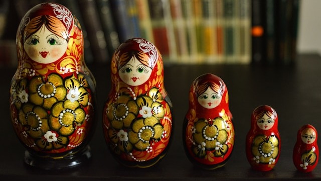 Cinco bonecas russas Matryoshka vermelhas, douradas e pretas, em fila, com tamanhos decrescentes.