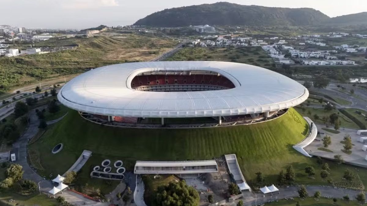 Estádio Akron, em Guadalajara Vista aérea de estádio oval branco, base verde com logo Chivas, estradas, prédios e colinas.
