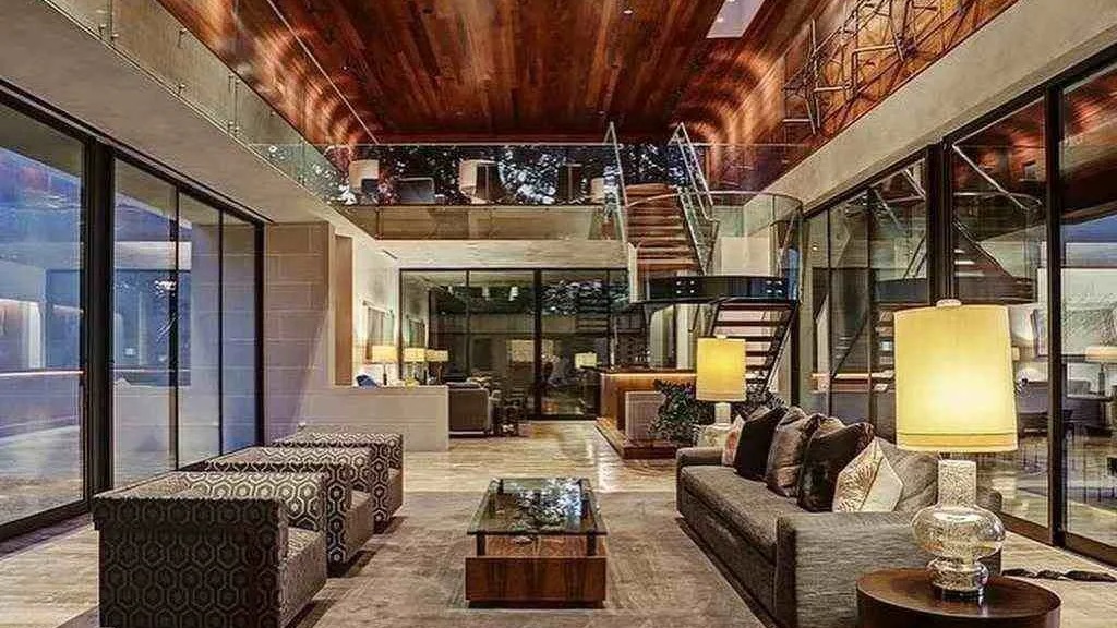 A mansão de Travis Scott em Houston, com seus espaços amplos e design moderno, reflete o luxo descrito na propriedade Interior de sala de estar luxuosa com teto alto, paredes de vidro e escada flutuante