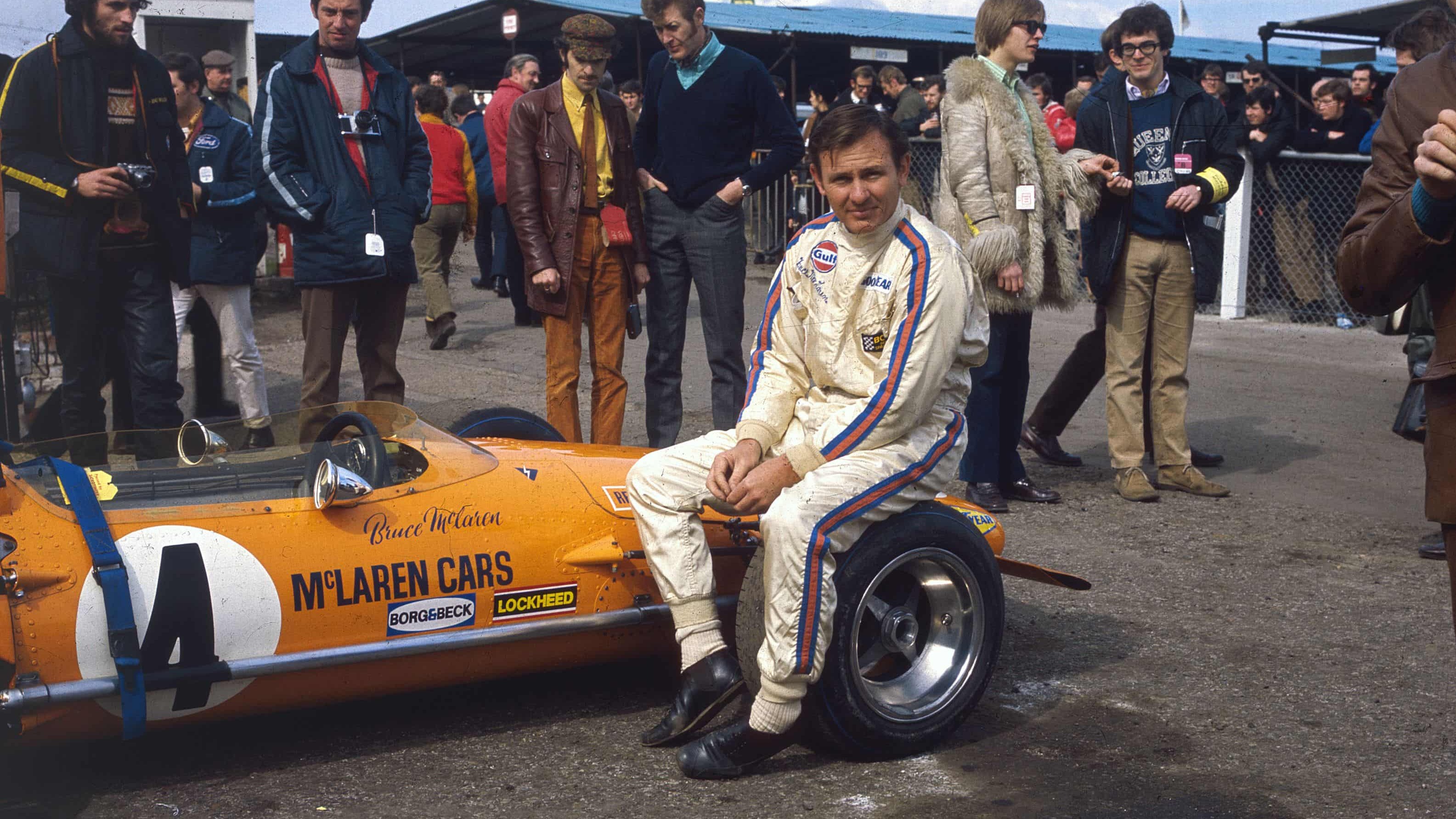 A imagem de Bruce McLaren sentado em seu carro de corrida, fonte da paleta de cores da nova identidade visual da McLaren. Bruce McLaren sentado em pneu de carro de corrida laranja, com logo MCLAREN CARS