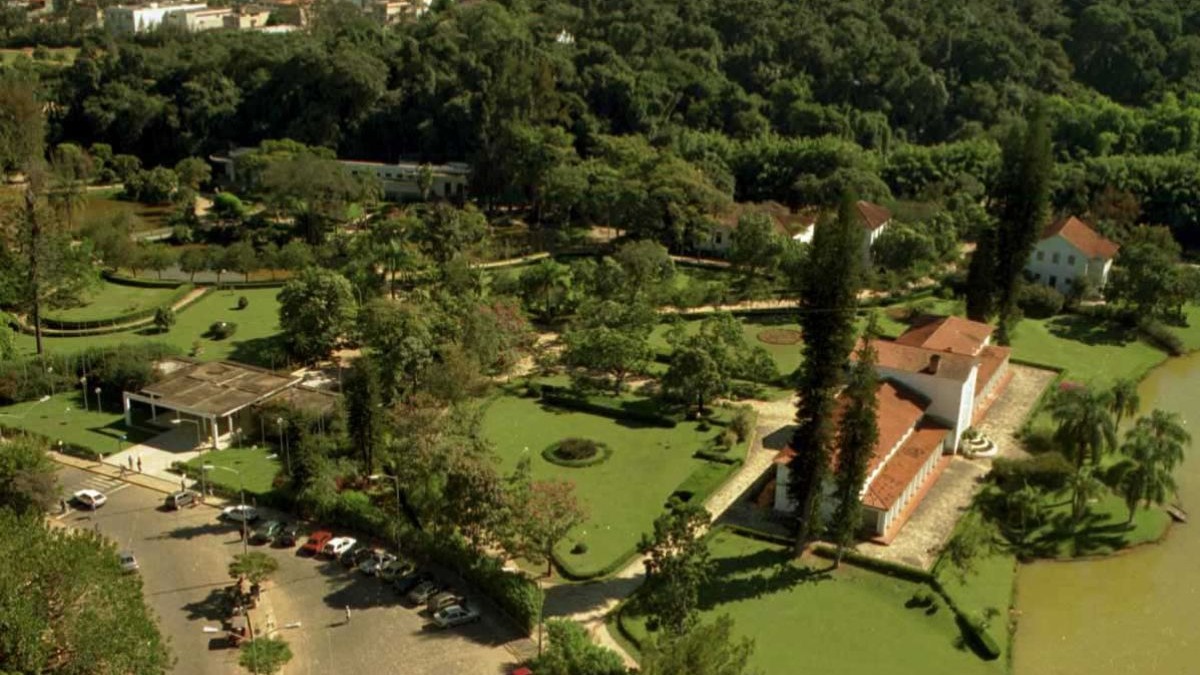 Vista a&eacute;rea de um parque com edif&iacute;cios, extensos gramados verdes, muitas &aacute;rvores e um lago.