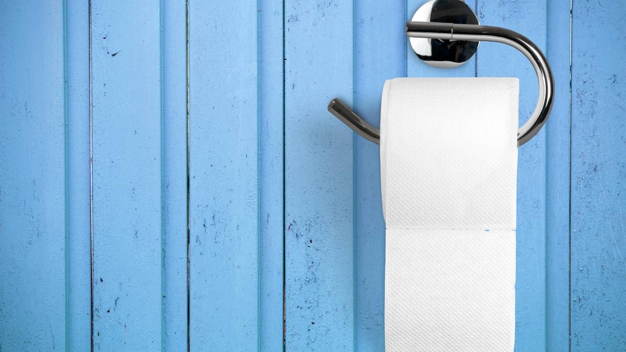 A orientação do papel higiênico com a ponta para a frente é a posição defendida pela patente histórica de Seth Wheeler Rolo de papel higiênico branco em suporte cromado fixado em parede de madeira azul