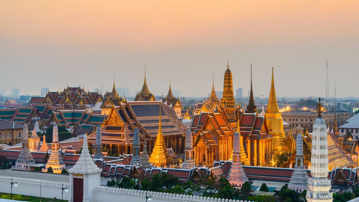 Vista a&eacute;rea de templos dourados e brancos com spires em Bangkok sob c&eacute;u crepuscular.