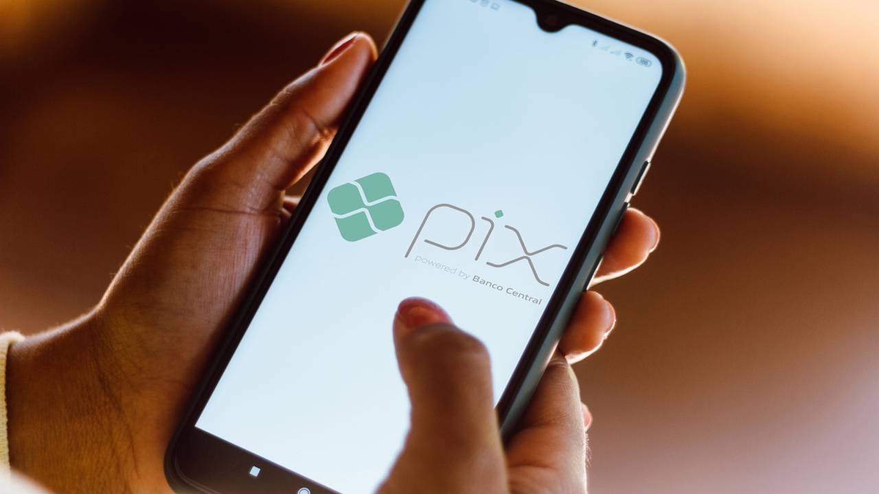 Com o Pix no celular, empreendedores otimizam vendas e facilitam pagamentos para seus clientes. Mão segura smartphone preto exibindo logo verde Pix e texto "powered by Banco Central".