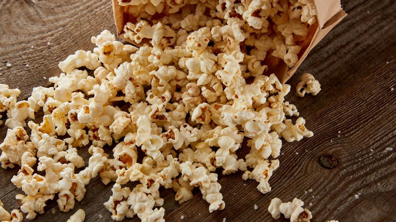 O milho estourado é o ingrediente principal para a infusão que dá o sabor característico ao sorvete de pipoca caseiro. Pipoca estourada derramada de um saco de papel pardo sobre uma superfície de madeira