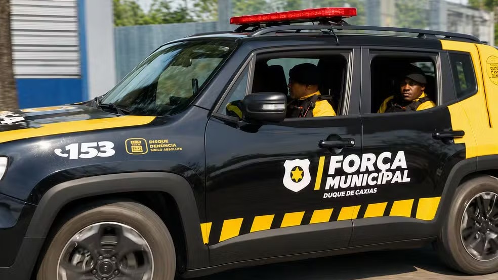Viatura da Força Municipal de Duque de Caxias patrulha as ruas em operação de segurança pública. Viatura preta e amarela da Força Municipal Duque de Caxias com dois guardas em movimento
