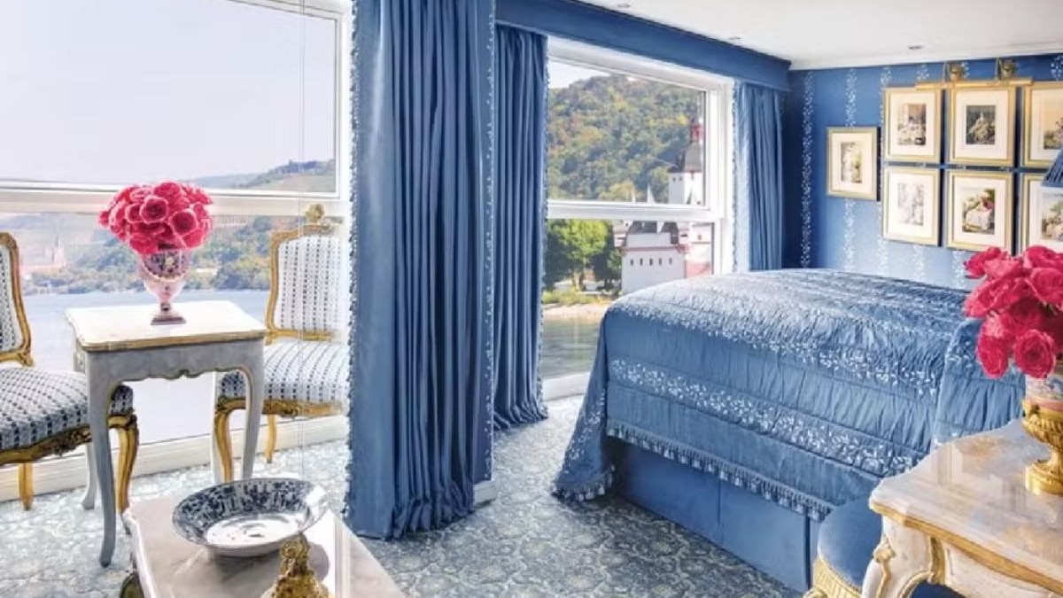 Quarto de navio luxuoso em tons de azul com cama, cortinas e vista para rio.