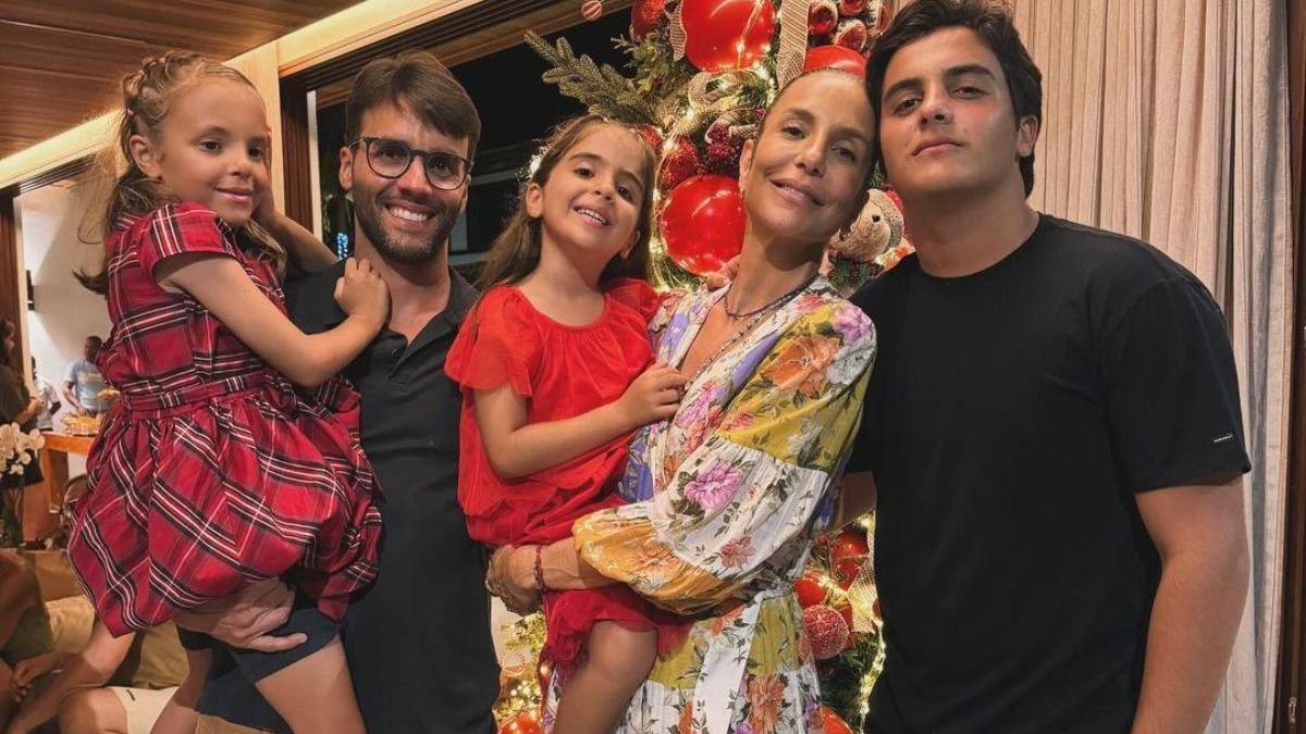 Daniel Cady ao lado dos filhos em um momento familiar, evidenciando o foco na alimentação e rotina saudável dos jovens Daniel Cady com óculos, uma mulher e três crianças sorrindo, em frente a uma árvore de Natal
