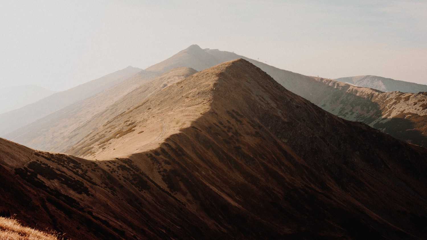 Cumes de montanhas com vegetação seca sob um céu claro e neblina sutil.