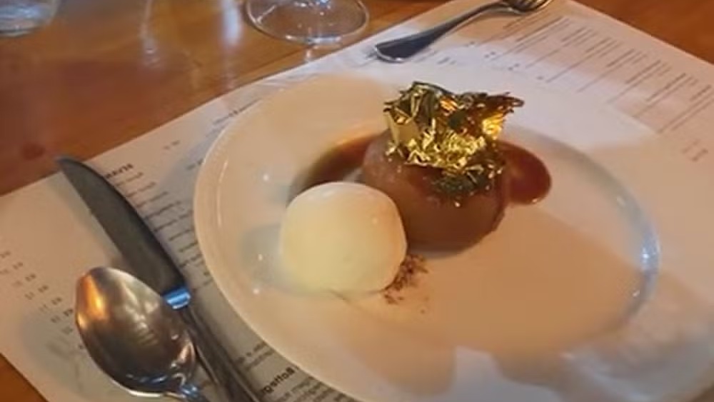 A sobremesa com folhas de ouro que Wanessa Camargo e Bruno Bevan compartilharam em seu jantar romântico, tema de brincadeiras do casal. Sobremesa em prato branco com fruta assada coberta de folhas de ouro e sorvete
