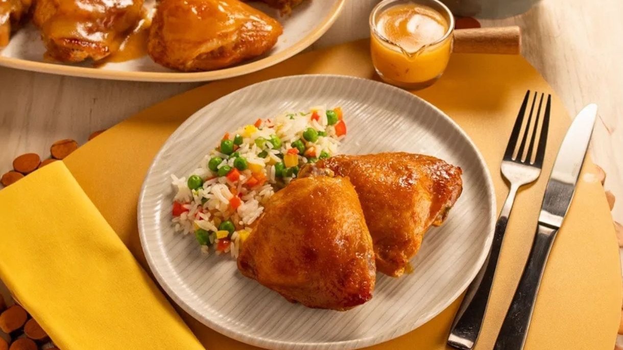 Duas sobrecoxas de frango douradas com molho e arroz primavera em prato branco.