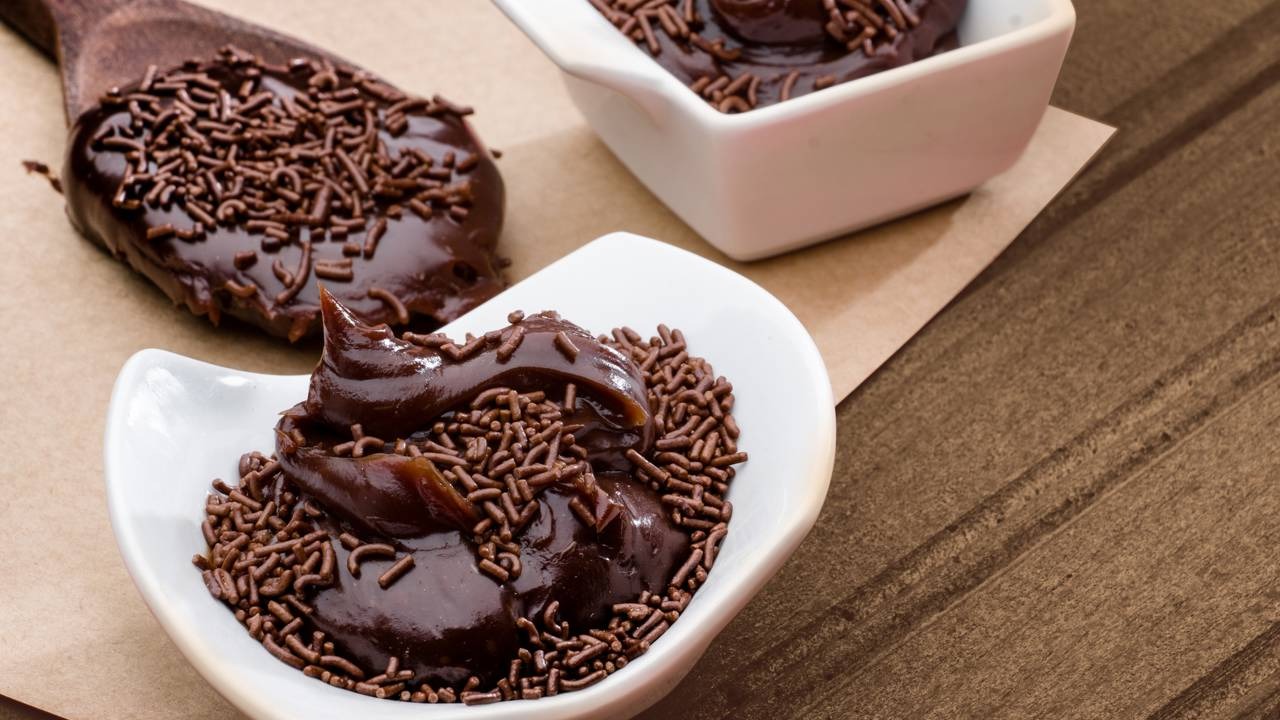 O brigadeiro de colher, com sua textura fluida, é destaque entre os tipos de doce prático e versátil. Brigadeiro de chocolate com granulado em tigelas brancas e colher de madeira
