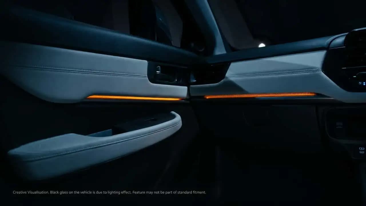 A cabine renovada do Honda Elevate se destaca pelo revestimento claro e iluminação ambiente alaranjada nos painéis. Interior de carro com painéis claros, iluminação ambiente laranja e detalhes costurados.