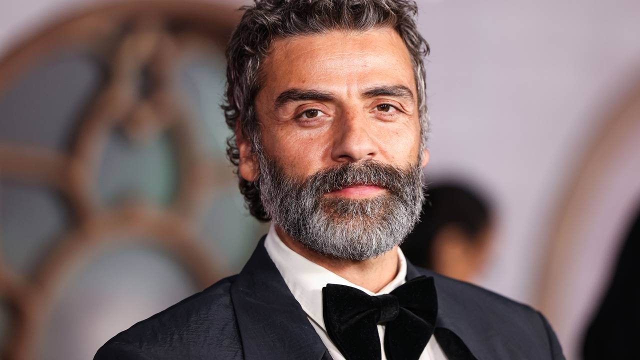 Oscar Isaac, que entregou uma performance aclamada em "Ecos de Júpiter", foi surpreendentemente esnobado nas indicações ao Oscar 2026. Oscar Isaac em close, cabelo e barba grisalhos, vestindo smoking preto e gravata borboleta.