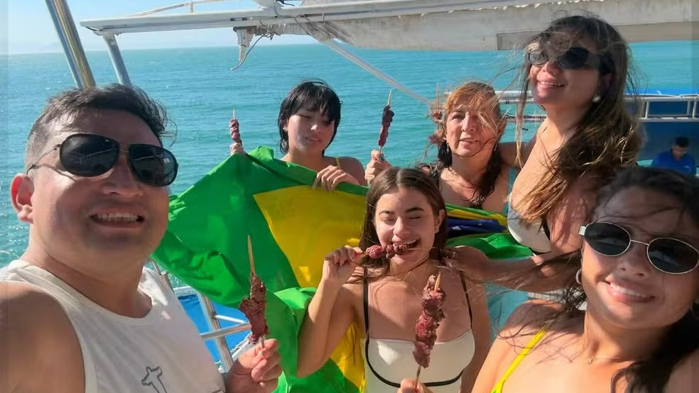 A alegria da família colombiana em um de seus passeios pelo Rio de Janeiro, com a bandeira do Brasil, antes da trágica queda do helicóptero. Foto: Reprodução Seis pessoas em barco com espetinhos, uma bandeira do Brasil e mar ao fundo