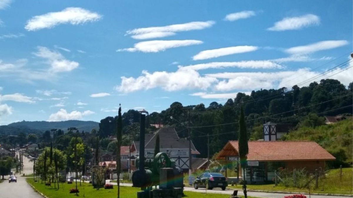 Monte Verde, na Serra da Mantiqueira, reflete a arquitetura europeia e o clima ameno dos destinos de serra mineiros. Rua com edifícios de arquitetura europeia, montanhas, céu azul, nuvens, carro e máquina antiga.