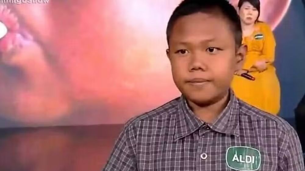Ardi Rizal, que superou o vício em nicotina, hoje compartilha sua experiência alertando sobre os perigos da dependência Jovem asiático de camisa xadrez, com crachá "ALDI", mulher desfocada ao fundo