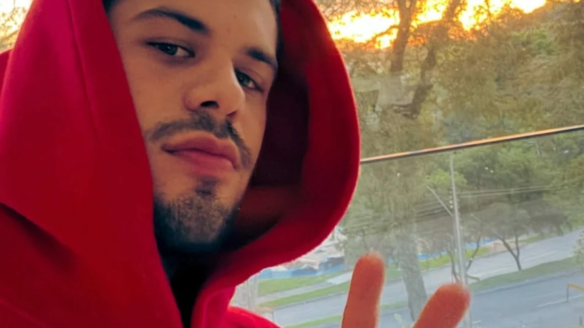 Zé Felipe em momento de concentração, conforme explicou sobre o isolamento para seu processo criativo de novas músicas. Zé Felipe em selfie, capuz vermelho, barba e mão com sinal de paz. Fundo desfocado.