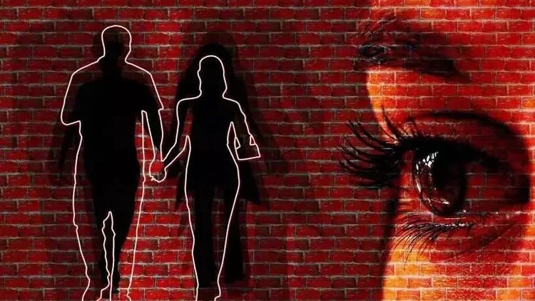 Silhuetas de casal de m&atilde;os dadas e olho chorando sobre parede de tijolos vermelhos