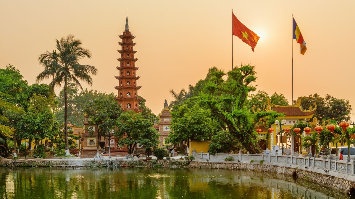 Pagoda de v&aacute;rias camadas, lago, &aacute;rvores verdes, bandeiras vietnamita e budista em Han&oacute;i ao p&ocirc;r do sol.