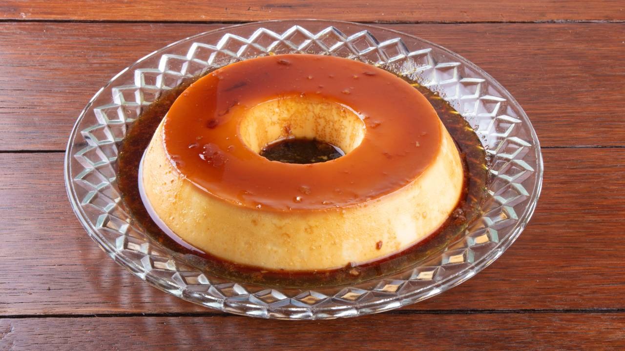 Pudim, um clássico da culinária que se tornou sucesso no TikTok, exemplifica a tendência das receitas práticas de Ana Maria Braga. Pudim de caramelo redondo e dourado em um prato de vidro sobre madeira