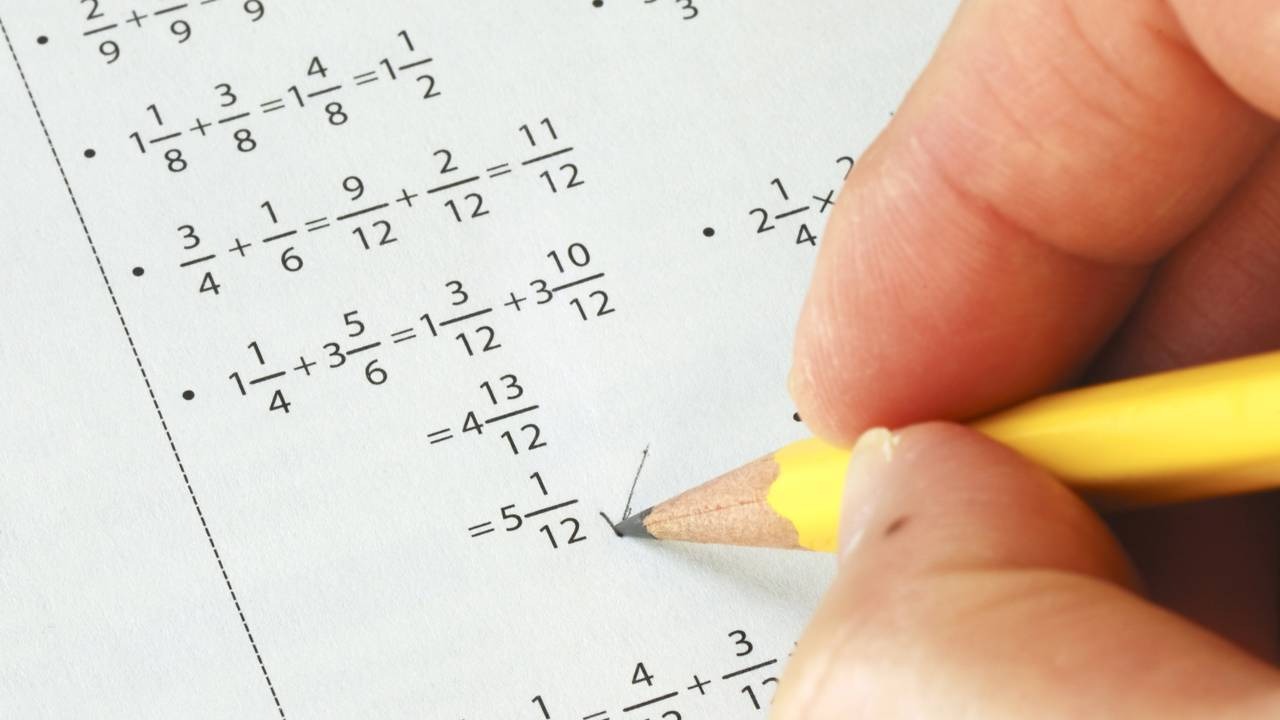 A falta de prática em cálculos matemáticos, como a adição de frações, pode levar ao esquecimento de regras básicas ao longo do tempo. Mão escreve com lápis em folha de papel com exercícios de matemática de frações