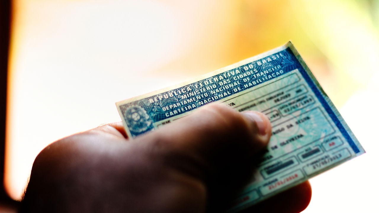 O programa Cidadania Sobre Rodas oferece a CNH gratuita para pessoas com deficiência, promovendo inclusão e independência no trânsito. Mão segura uma CNH azul com texto 'REPUBLICA FEDERATIVA DO BRASIL' e datas visíveis.