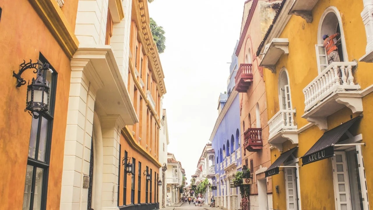 Ruas coloridas de Cartagena, na Colômbia, um dos destinos que brasileiros podem visitar sem visto em 2026 Rua estreita com edifícios coloniais coloridos e pessoa em varanda ornamentada