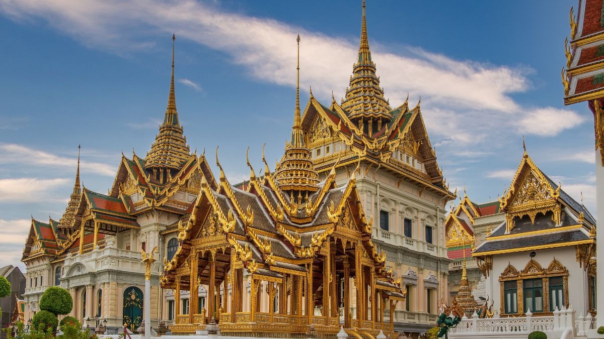 Complexo de templos dourados e brancos com telhados pontiagudos em Bangkok sob c&eacute;u azul.