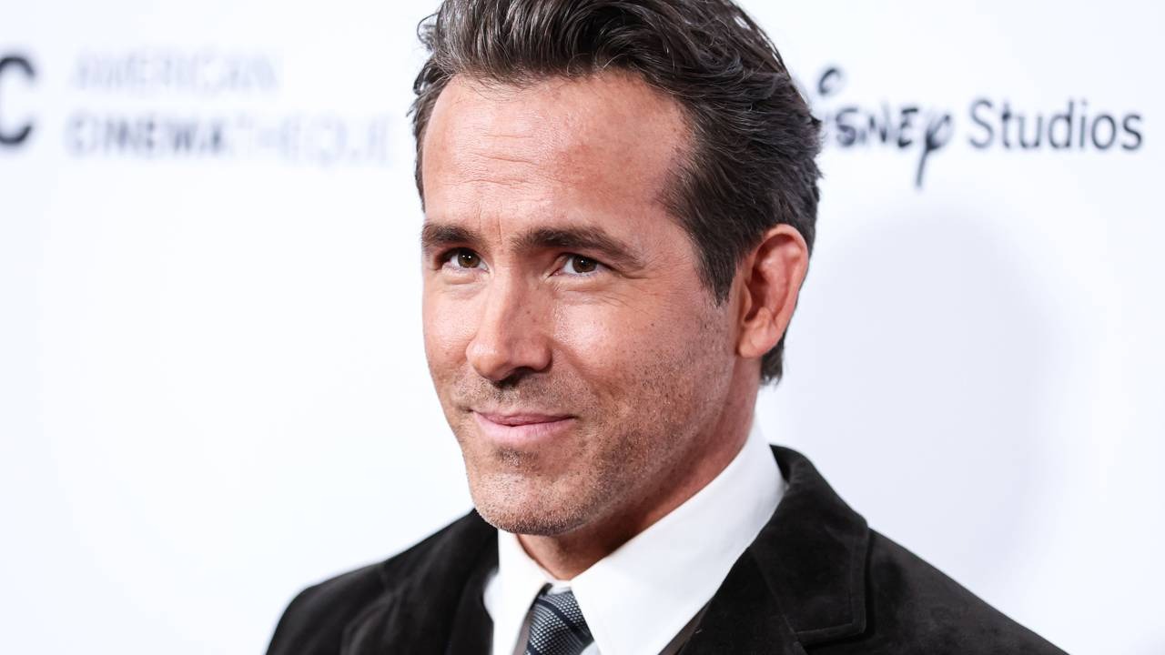 Ryan Reynolds, ator do filme Lanterna Verde de 2011, não faz parte do elenco da nova série 'Lanternas'. Close-up de Ryan Reynolds, cabelo escuro e barba, vestindo terno e gravata