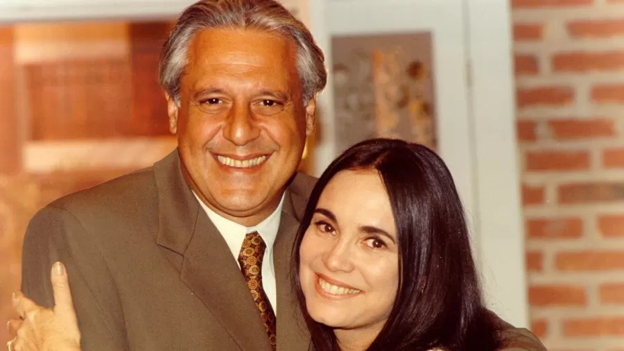 Antonio Fagundes e mulher sorrindo, abraçados, em close-up, fundo desfocado de tijolos.