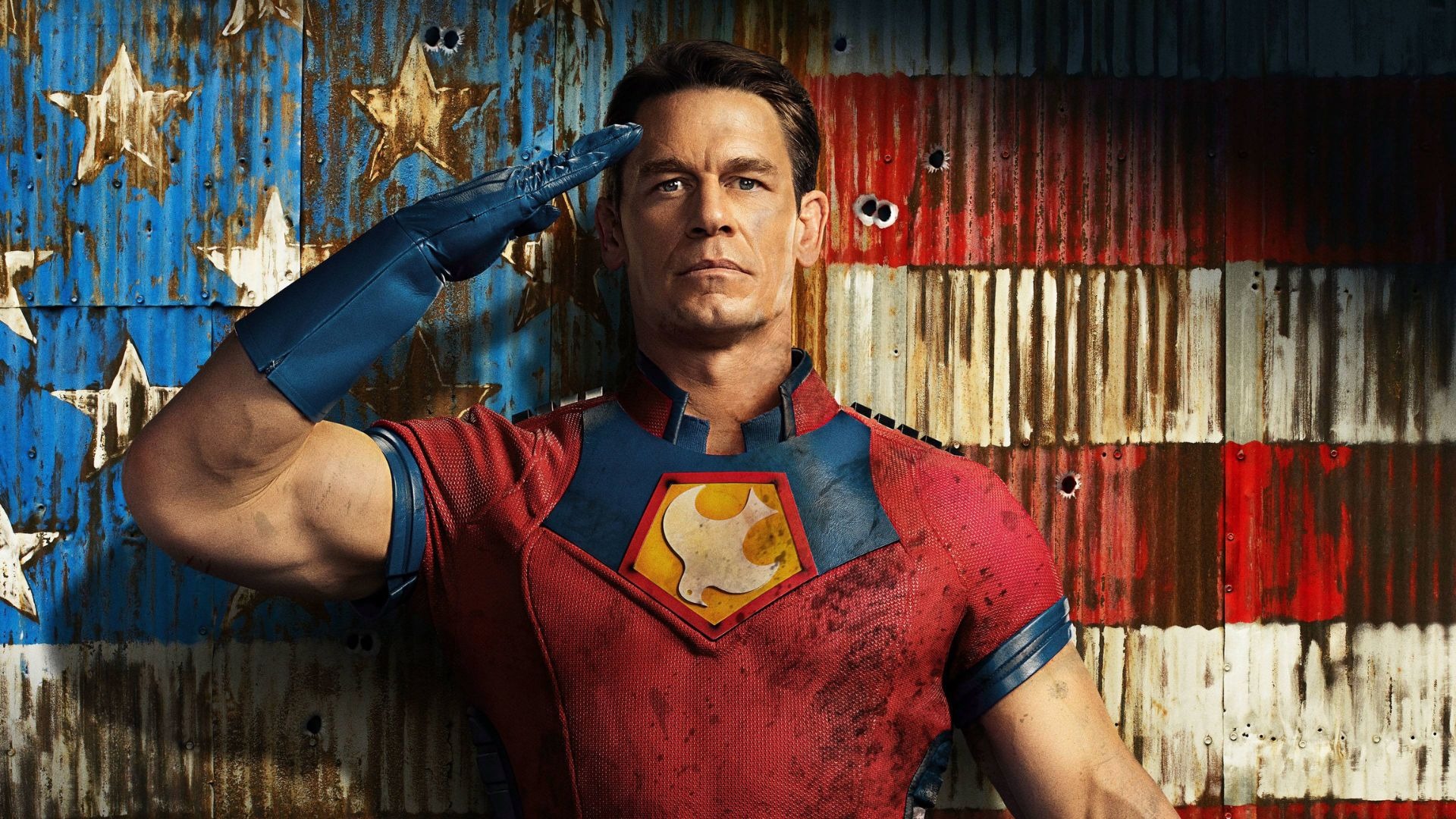 John Cena como Pacificador, anti-herói brutal e carismático, em destaque na lista de séries para quem amou "The Boys". John Cena, como Pacificador, uniforme vermelho e azul, fazendo continência, fundo de bandeira EUA desgastada.
