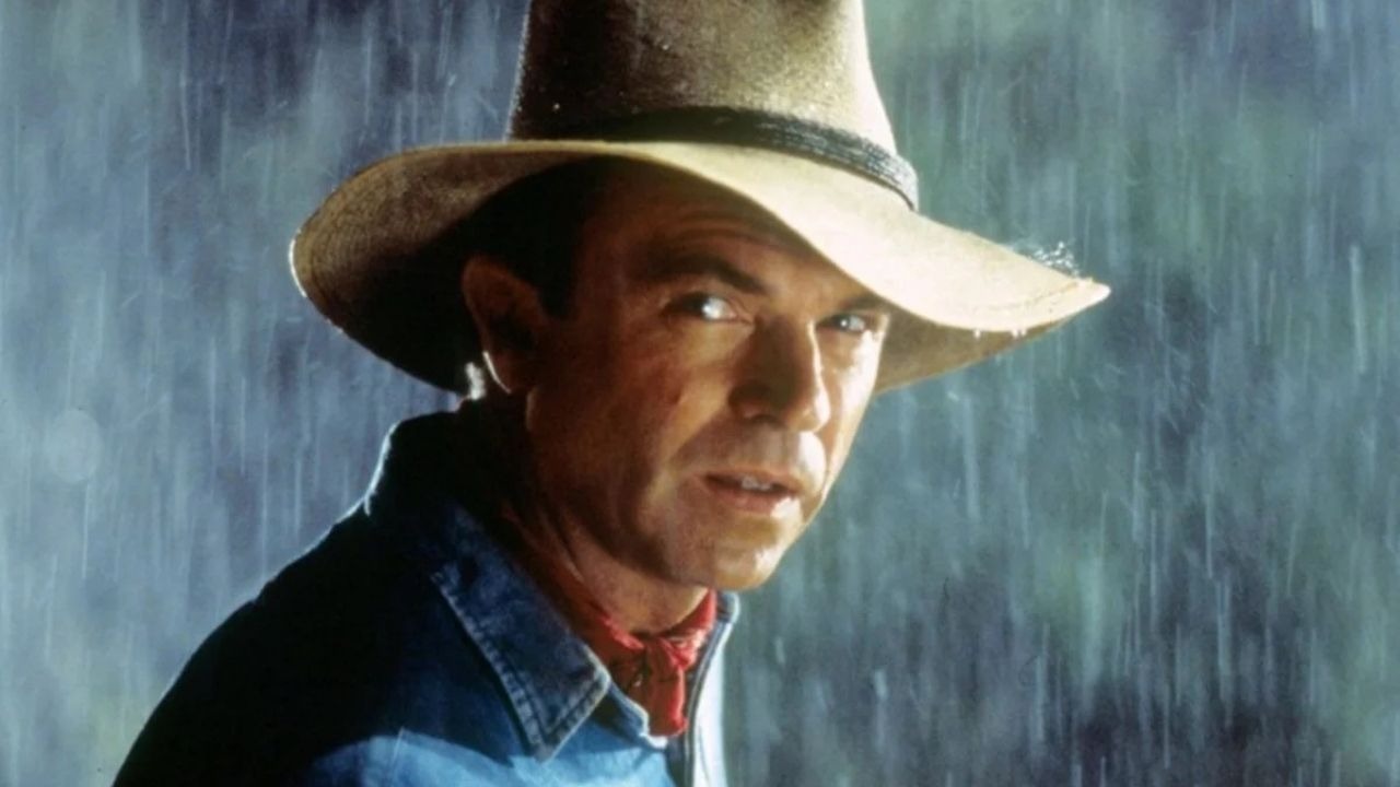 Sam Neill no papel de Alan Grant em "Jurassic Park", um dos trabalhos que o imortalizaram no cinema. Ator Sam Neill, com chapéu e camisa jeans, sob chuva, olhando por cima do ombro