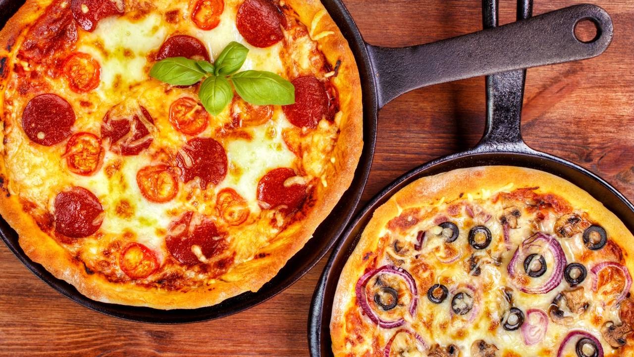 Pizzas feitas diretamente na frigideira são uma opção prática e saudável, ideais para um preparo rápido em casa. Duas pizzas em frigideiras, uma de pepperoni e outra com cogumelos, cebola e azeitona