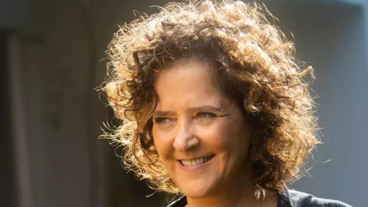Retrato de mulher sorrindo, com cabelo cacheado castanho-claro, iluminado por trás, em close-up.